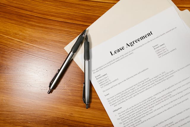 a-lease-agreement-document-on-a-wooden-surface-partially-inside-a-folder-with-two-pens-placed-beside-it a-lease-agreement-document-on-a-wooden-surface-partially-inside-a-folder-with-two-pens-placed-beside-it